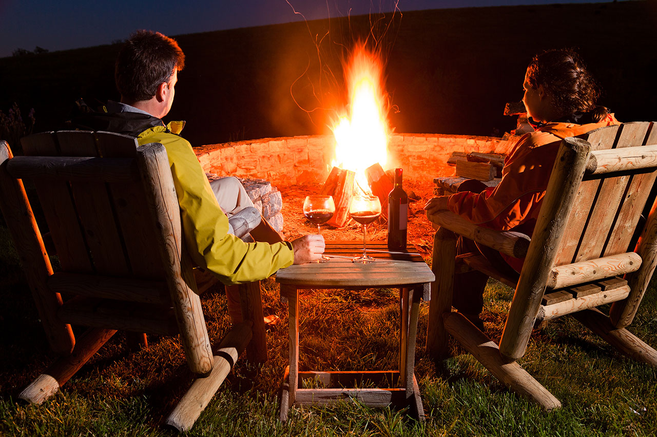 Couple with wine sitting by a campfire.